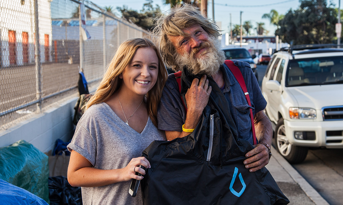 A student giving a jacket to a homeless person