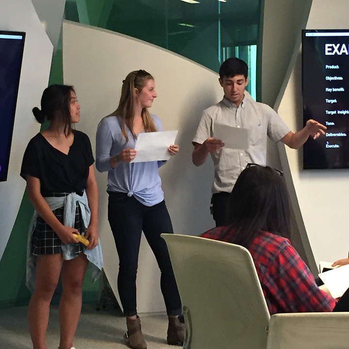Three students giving a presentation in front of several LCD screens