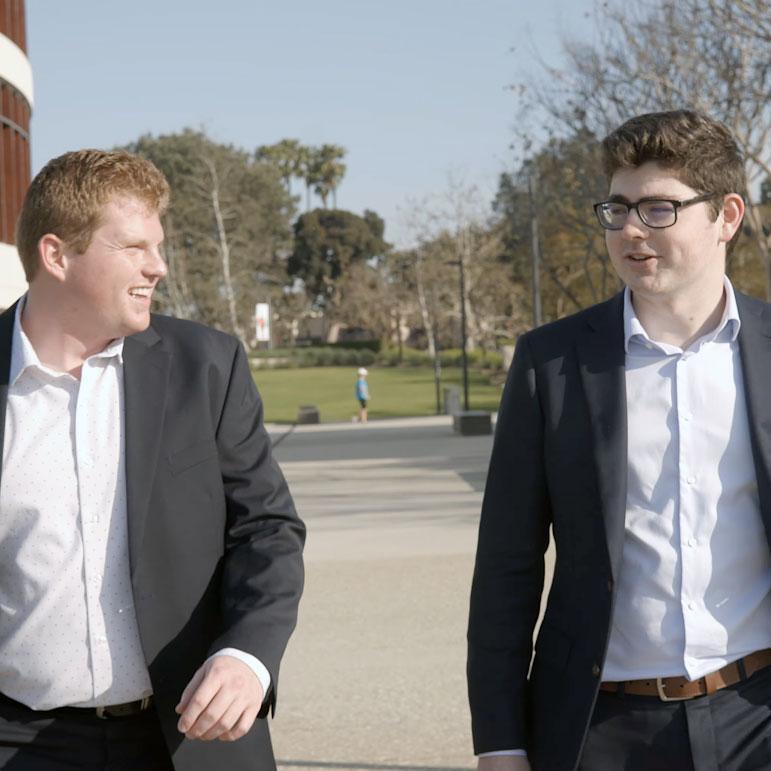 Alums Liam Wall and Sam Camper walking past the LMU William H Hannon Library