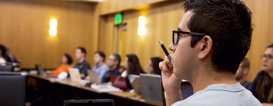 Professionally dressed students seated at a large round table listening to a lecture