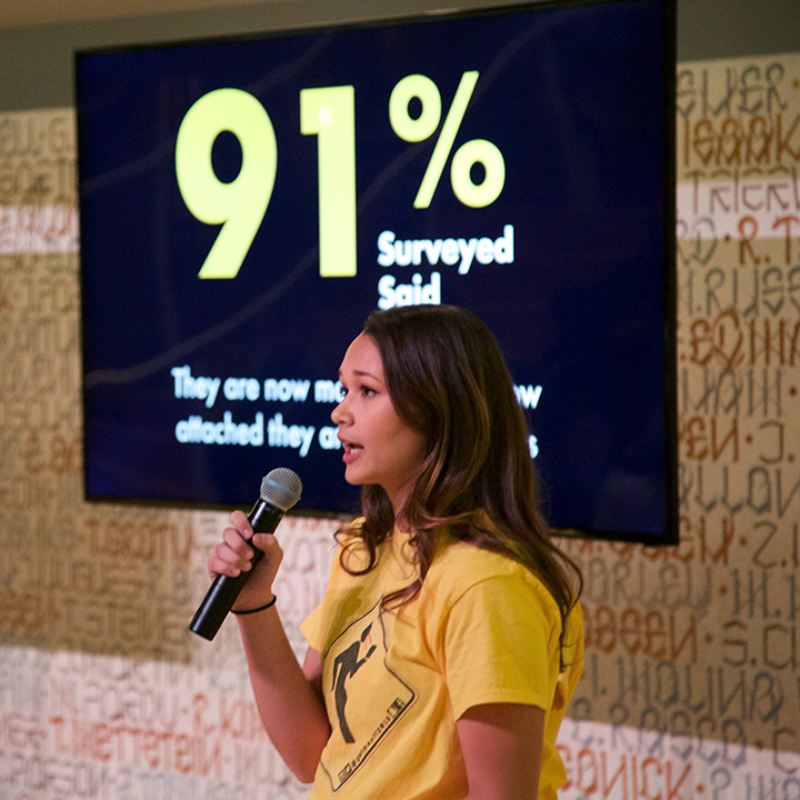 A student giving a presentation in front of an LCD screen listing information