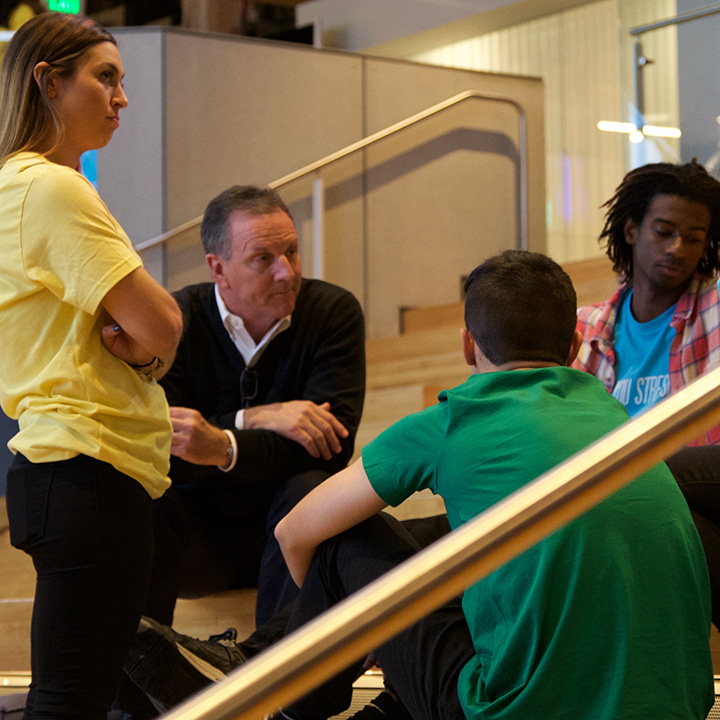 Three students seated around and speaking to an instructor