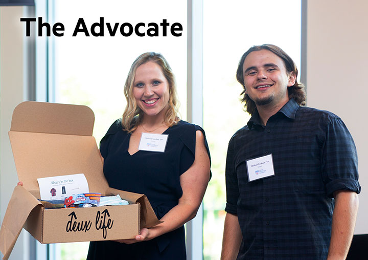 Two students showing a box with their proposed product packaged into it at an event with the words The Advocate